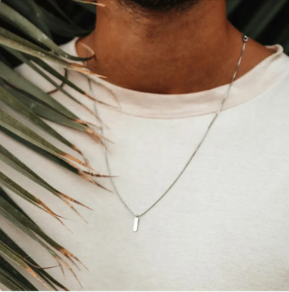 Man wearing a stainless steel clavicle chain necklace against a palm leaf backdrop.
