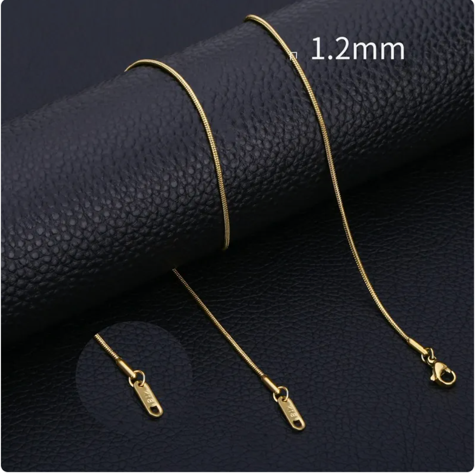 Minimalist stainless steel snake chain necklace in gold, showcasing a smooth design on a textured black surface.